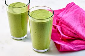 two tall pint glasses filled with green smoothie next to hot pink napkin