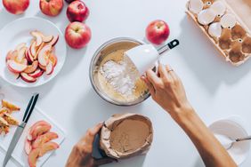 a flatlay of a person baking an Apple Pie and pouring flour into the dry ingredients
