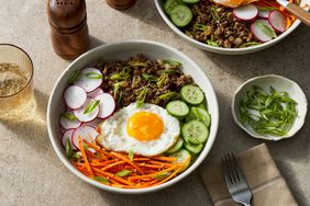 Bibimbap-inspired rice bowls recipe in a white bowl, with a cloth napkin a fork next to it, as well as a bowl of sliced scallions