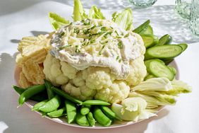 creamy loaded cauliflower dip surrounded by snap peas, fennel, cucumbers, potato chips