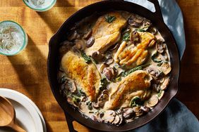 Creamy skillet chicken with spinach & mushrooms recipe, in a cast iron skillet, placed on a wooden surface and a light blue cloth napkin