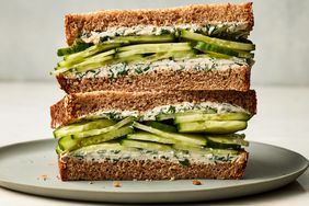 A cross section view of a sandwich on whole-wheat toast, filled with a cream cheese dill spread and sliced cucumbers