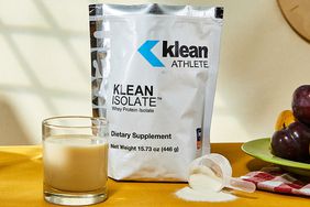 Klean Athlete Klean Isolate Protein Powder on yellow table next to prepared drink and spilled powder