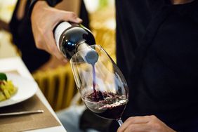 person pouring red wine into a glass