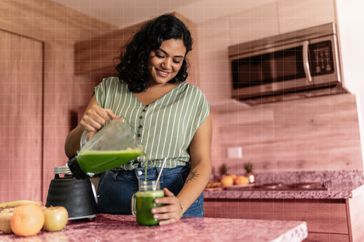 a photo of a woman pouring her smoothie from the blender into a drinking glass