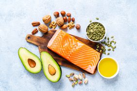 a photo of a cutting board with salmon, avocado, nuts, seeds, and olive oil
