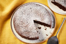 One-bowl chocolate cake, on a white plate on a yellow cloth background, with one slice of the cake cut out and put on another cake