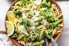 overhead shot of brown bowl filled with rotini pasta, broccoli, parmesan and lemon slices