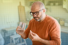 a photo of a man taking pill holding a glass of water