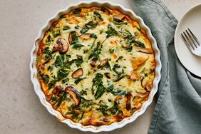 Spinach & Mushroom quiche in a white fluted dish with a linen and small plate on a light surface.