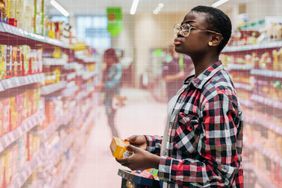 a photo of a woman looking at the various foods in the grocery aisle while holding a product